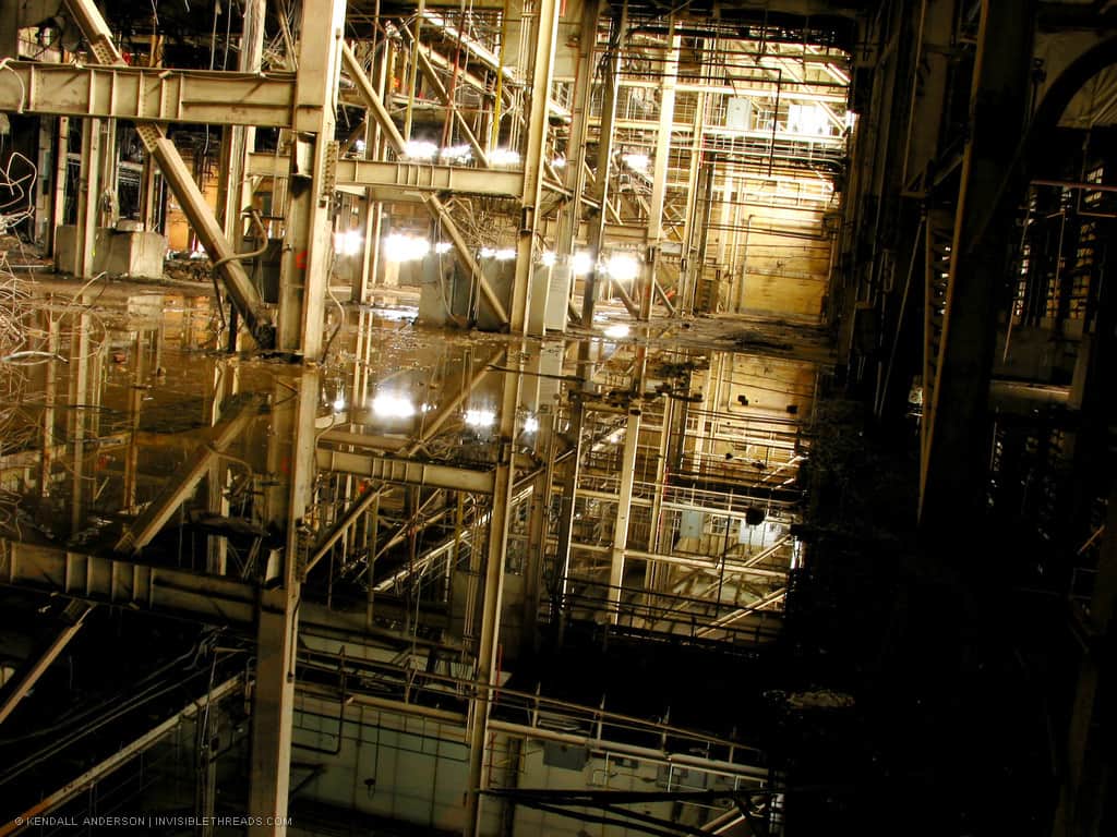 The ground floor interior of a large industrial power station is flooded with water. The water shows the reflection of the steel columns and beams inside.
