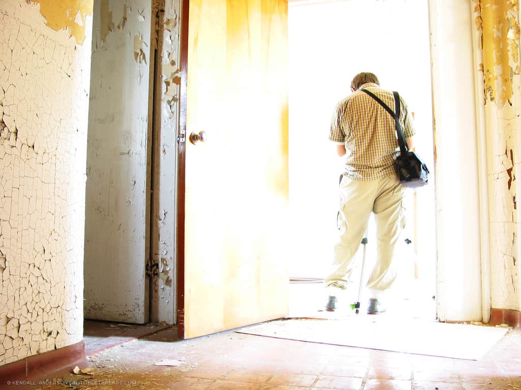 A person stands in a bright doorway. Walls are covered in peeling and cracking paint.