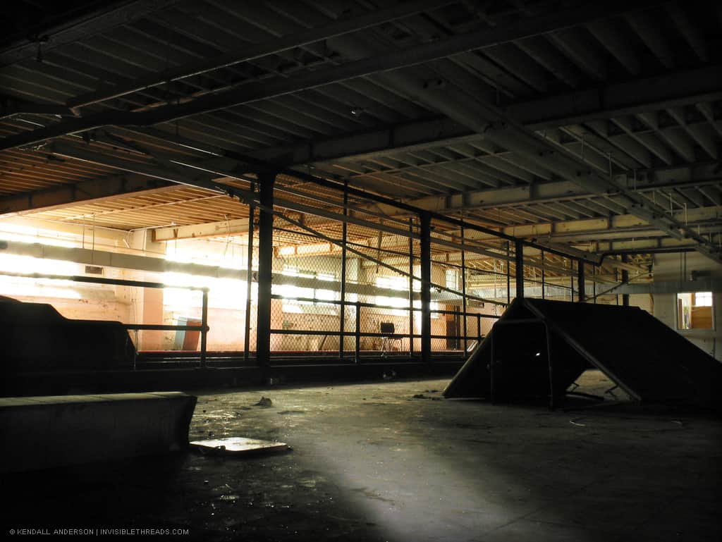 The basement of a gymnasium building is separated in two with a chain link fence which extends to the ceiling.