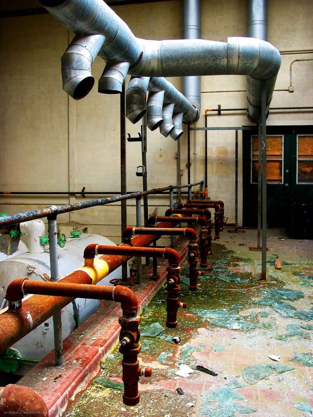 An array of silver metal air ducts is positioned about an array of red pipes. The floor is covered in debris.
