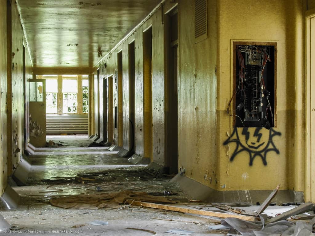 A bright yellow corridor has debris strewn about the floors and graffiti on the walls.
