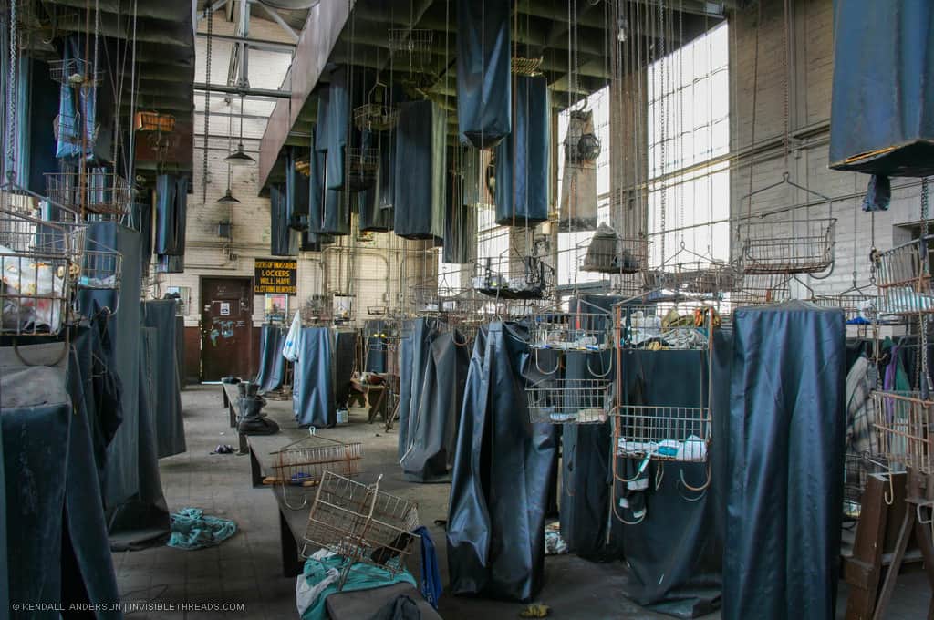 Rows of bags and baskets hang on chains from the ceiling. Some are hoisted to the ceiling, and others are at ground level. Many baskets are empty while some still contain personal items from former workers.