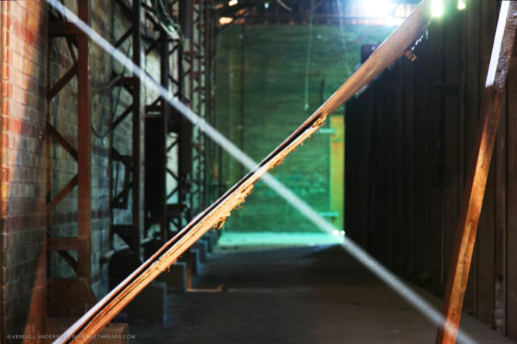 Factory corridor blocked by sheet of plywood, with light sunbeam in front creating an 'X' pattern