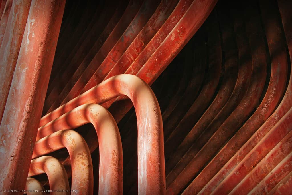 Multiple red pipes are grouped together, into 4 distinct groups. The pipes curve and bend together, forming an abstract pattern and texture.