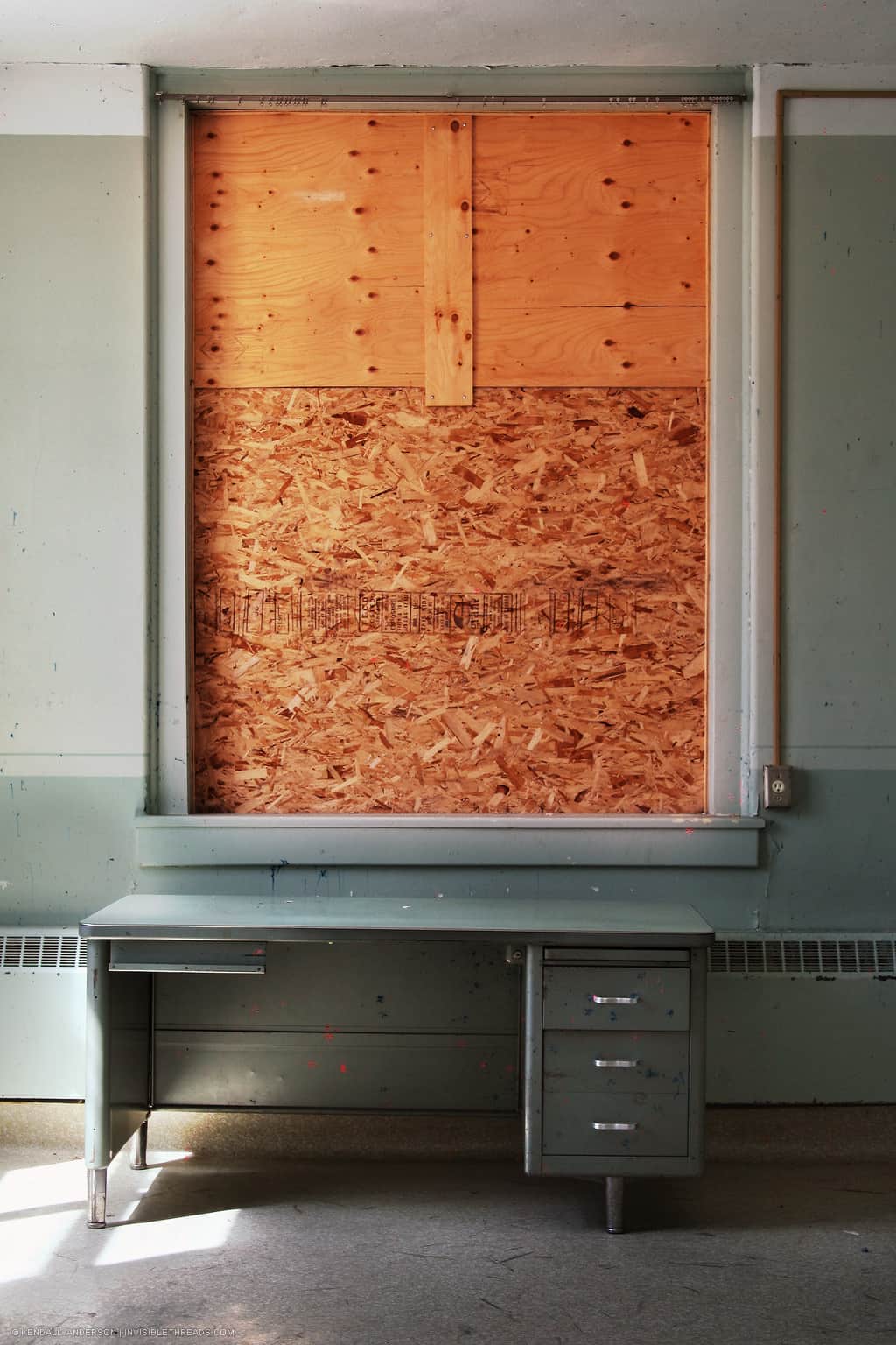 Metal office desk in front of a window that is completely boarded up with plywood