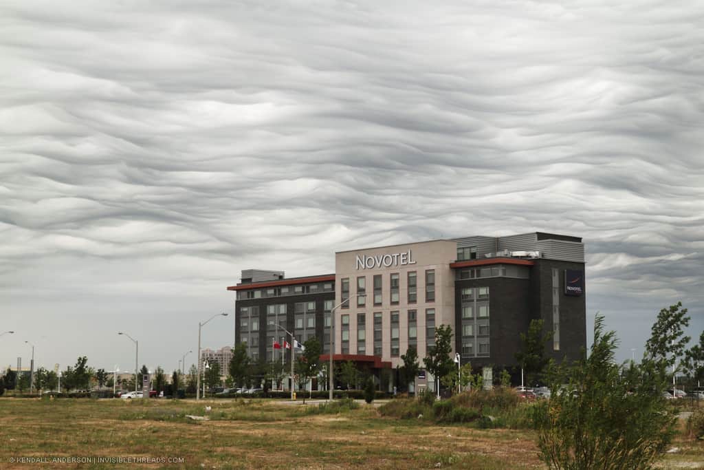 A 6-storey hotel building in the landscape, with wavy smoky cloud patterns in the sky beyond.
