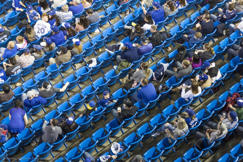 Blue baseball bleachers seen from above, half filled with people waiting for the game to begin