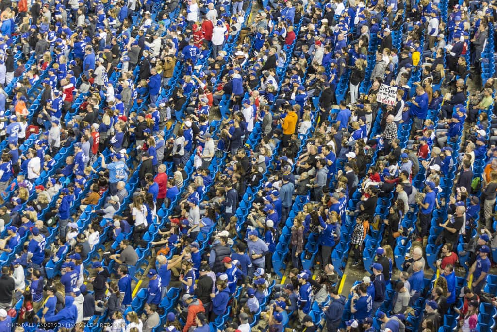 Hundreds of blue baseball bleacher seats with crowds of people sitting and standing, watching a baseball game