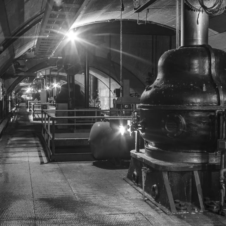 An arched passage contains industrial equipment used for hydroelectric turbines and generators. This passage is underground below the main turbine hall.