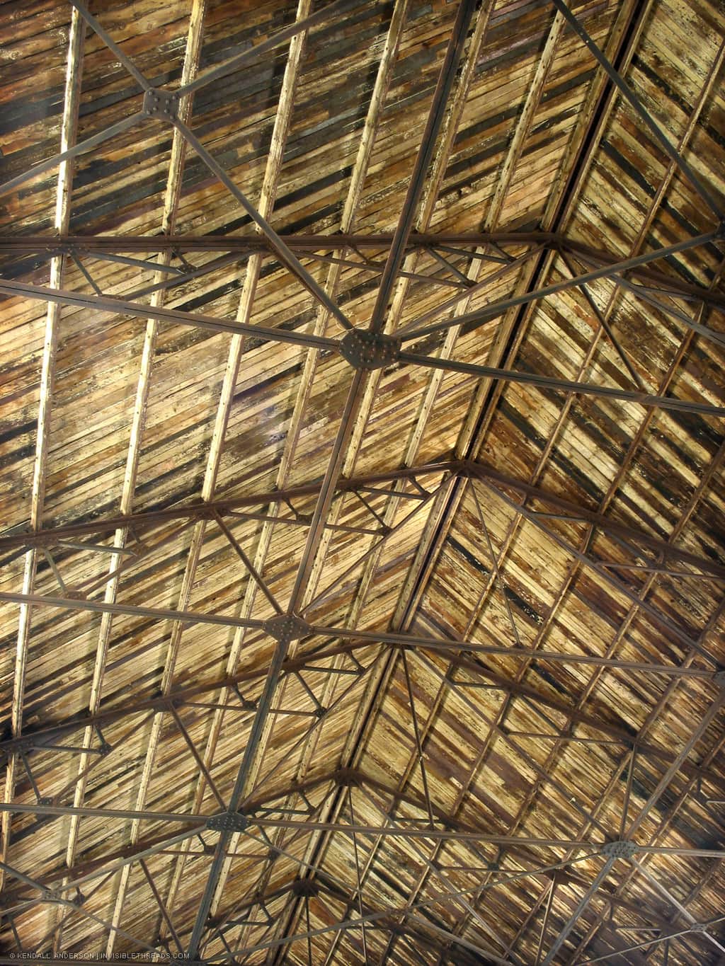 Underside of an industrial warehouse ceiling, with steel trusses supporting a wood slat roof