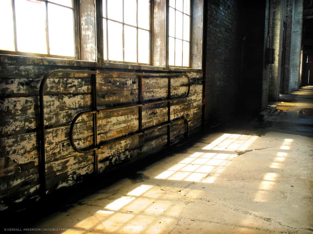 Light patterns from small square windows on dirt floor of empty industrial warehouse