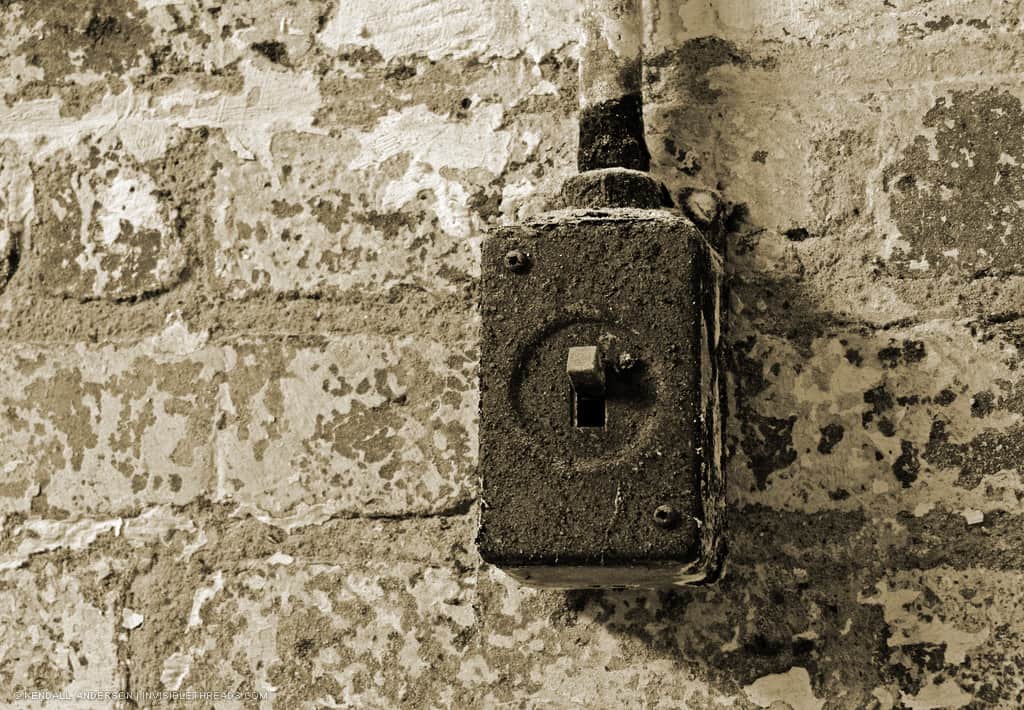 A dust covered light switch is mounted to an old brick wall.