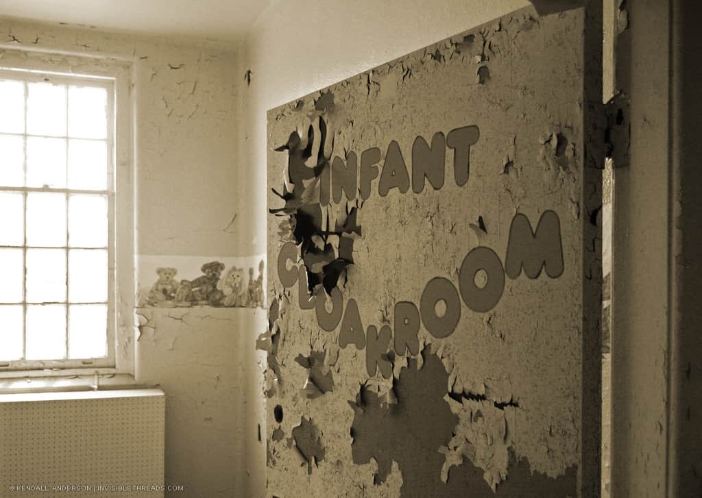 A door with peeling paint has the words 'Infant Cloakroom' painted on it.