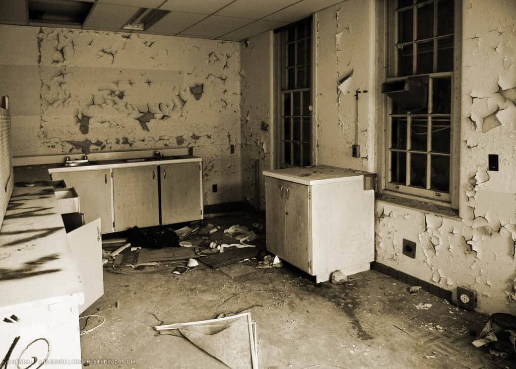 An abandoned kitchen is covered with debris. The walls are cracking and peeling.