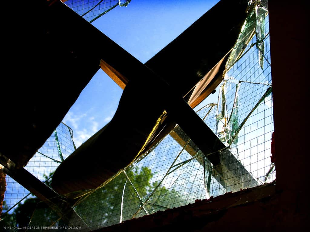 A chair is wedged inside a window frame, with broken glass all around it.