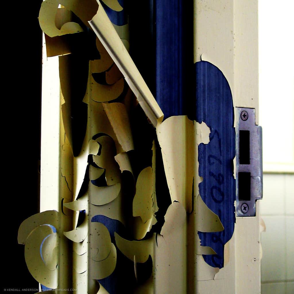 The white paint on a door frame is peeling off, revealing large sections of blue paint below.