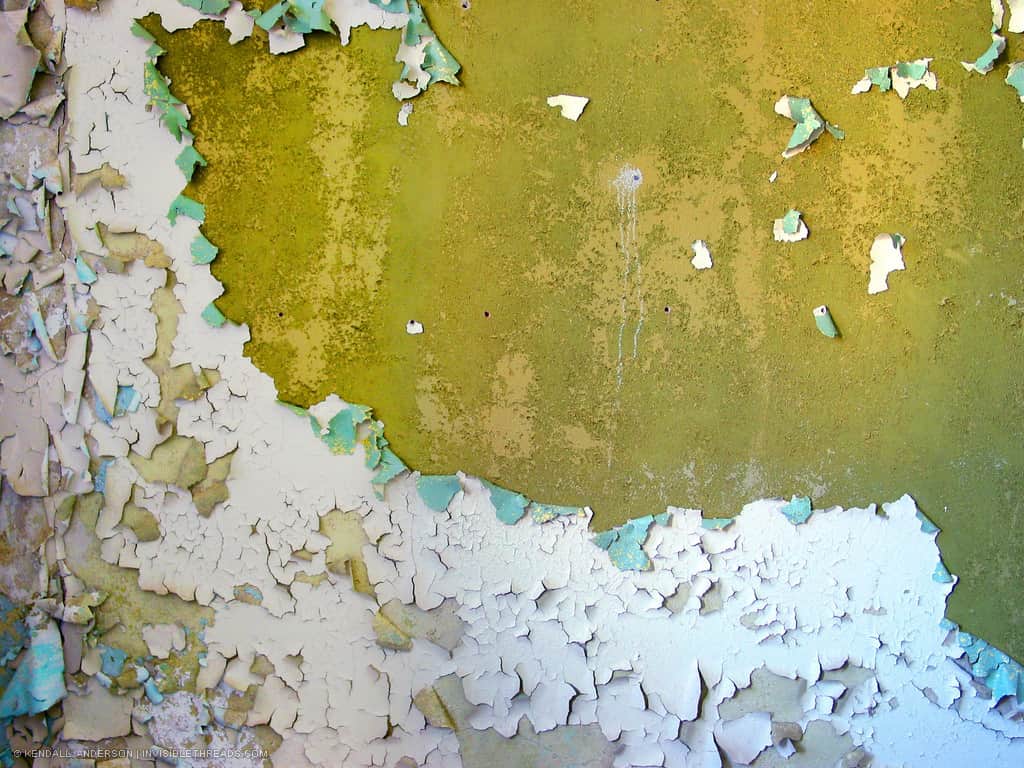 A wall is covered is flaking and peeling white paint.