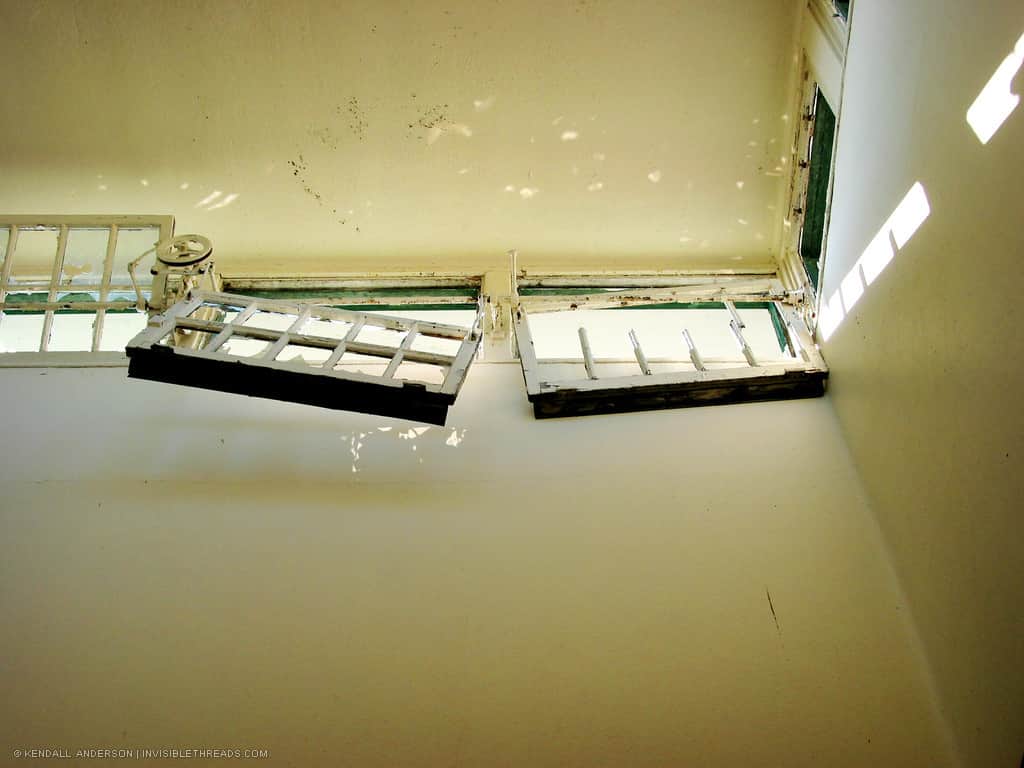 Near the ceiling of a yellow room are damaged skylight windows on broken hinges.