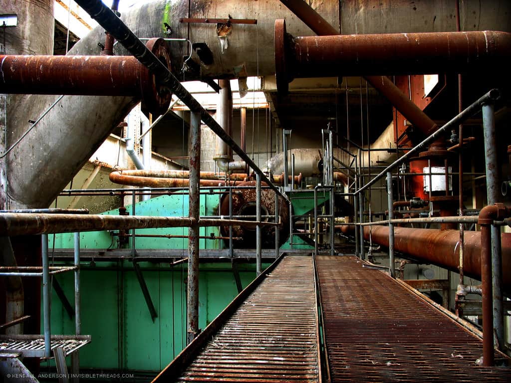 A series of pipes are at the end of a rusting metal catwalk.