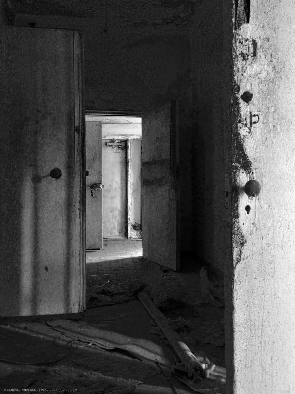 A dark corridor has a number of large doors which lead to washing or showering rooms.
