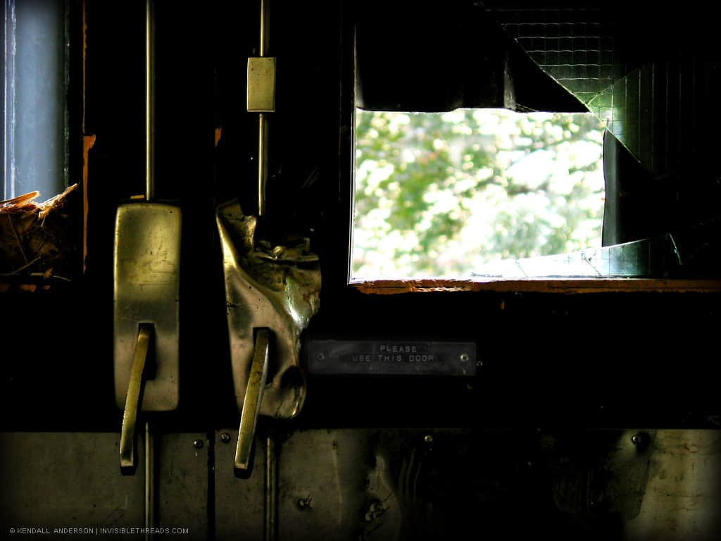 Two doors with push bars are broken and boarded up. The glass in one of the doors is broken.