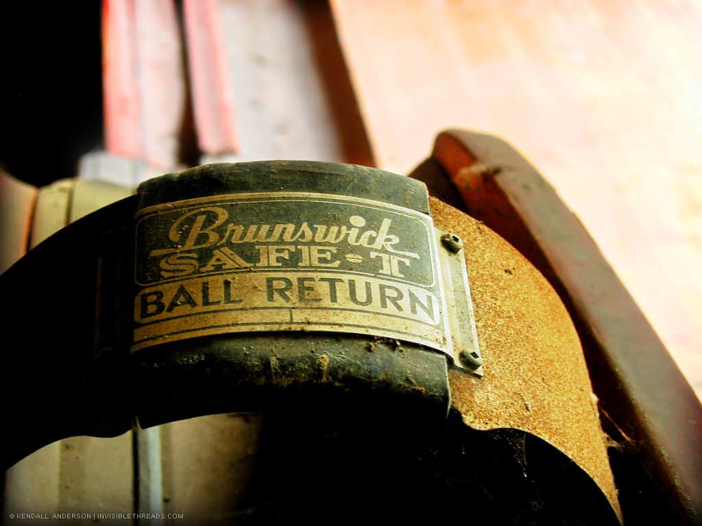 The metal plate on a bowling ball return channel reads, 'Brunswick Safe-T Ball Return'.