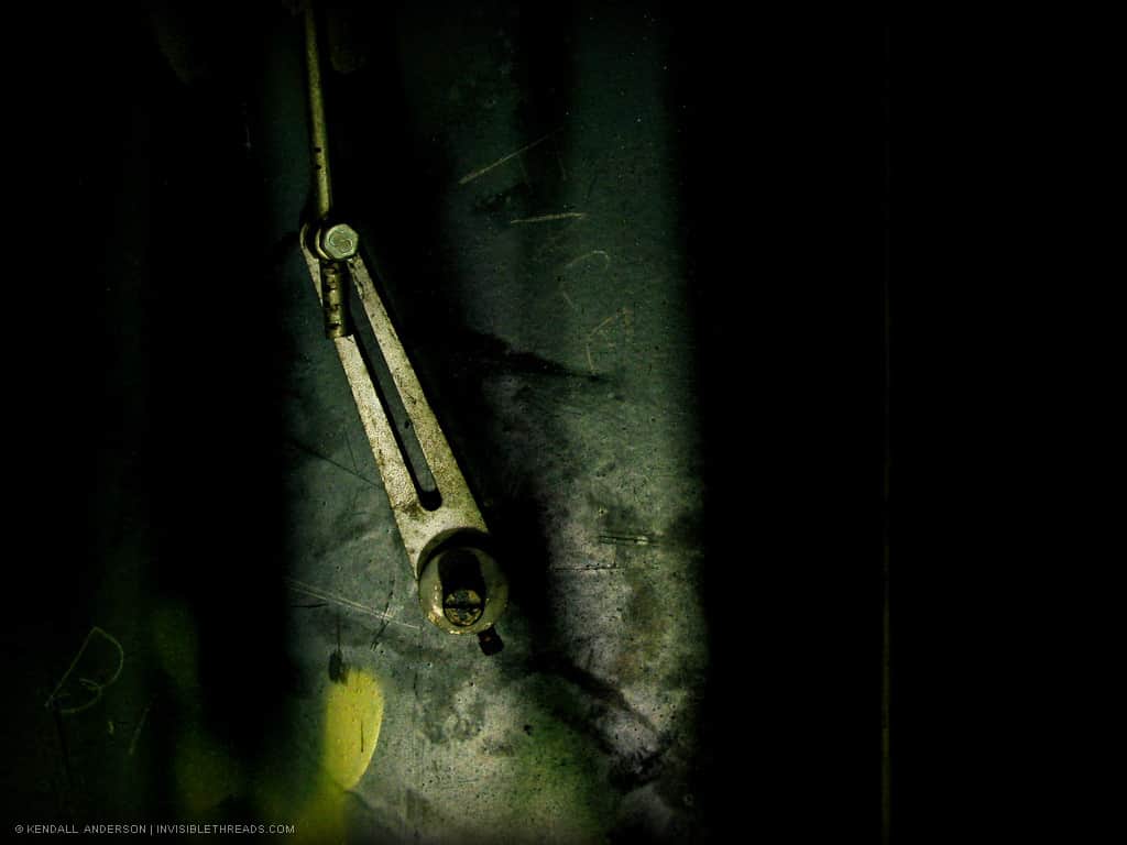 A metal bar connects to a metal latch, mostly in the dark.