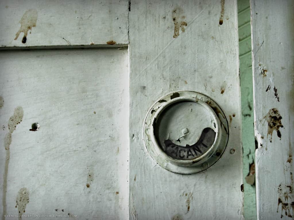 A 'Vacant' sign is visible on the exterior of a grimy wooden bathroom stall.