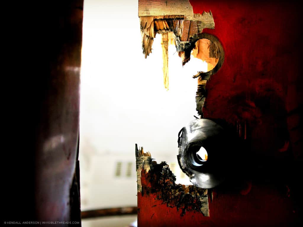 The remains of a red wood door show where the lock plate has been blasted off.