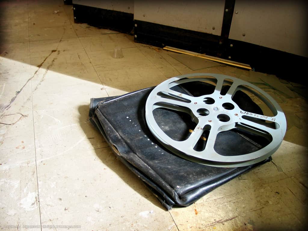 An empty circular film reel is lying on top of a leather case on the floor.
