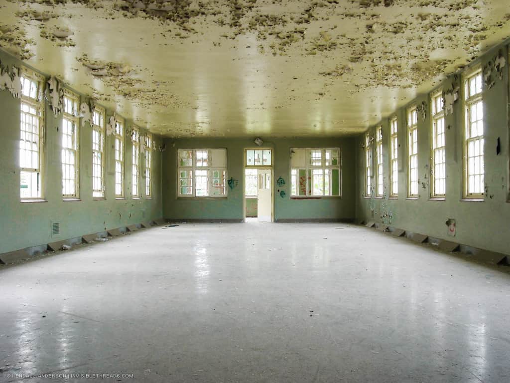 A bright green room is lined with windows. The floor is clean, but the ceiling is covered in peeling paint.