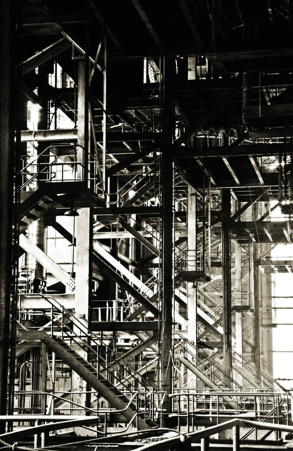 A high contrast view of the power station interior mixes arrays of columns and beams with stairs climbing up through about 5 storeys inside the building. Multiple stairwells recede into the distance towards the far wall of the building.