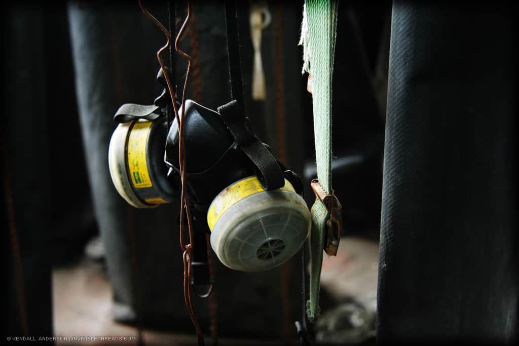 A safety respirator mask with yellow cartridges hangs from its straps in the employee change room.