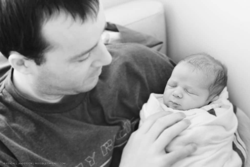 Man holding sleeping baby, swaddled in blanket