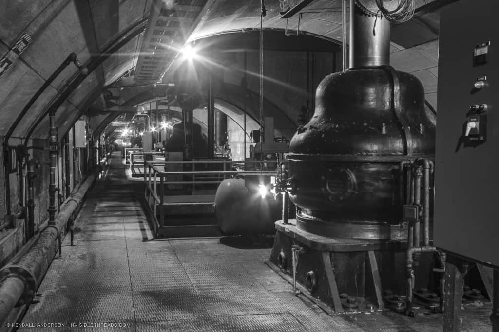 An arched passage contains industrial equipment used for hydroelectric turbines and generators. This passage is underground below the main turbine hall.