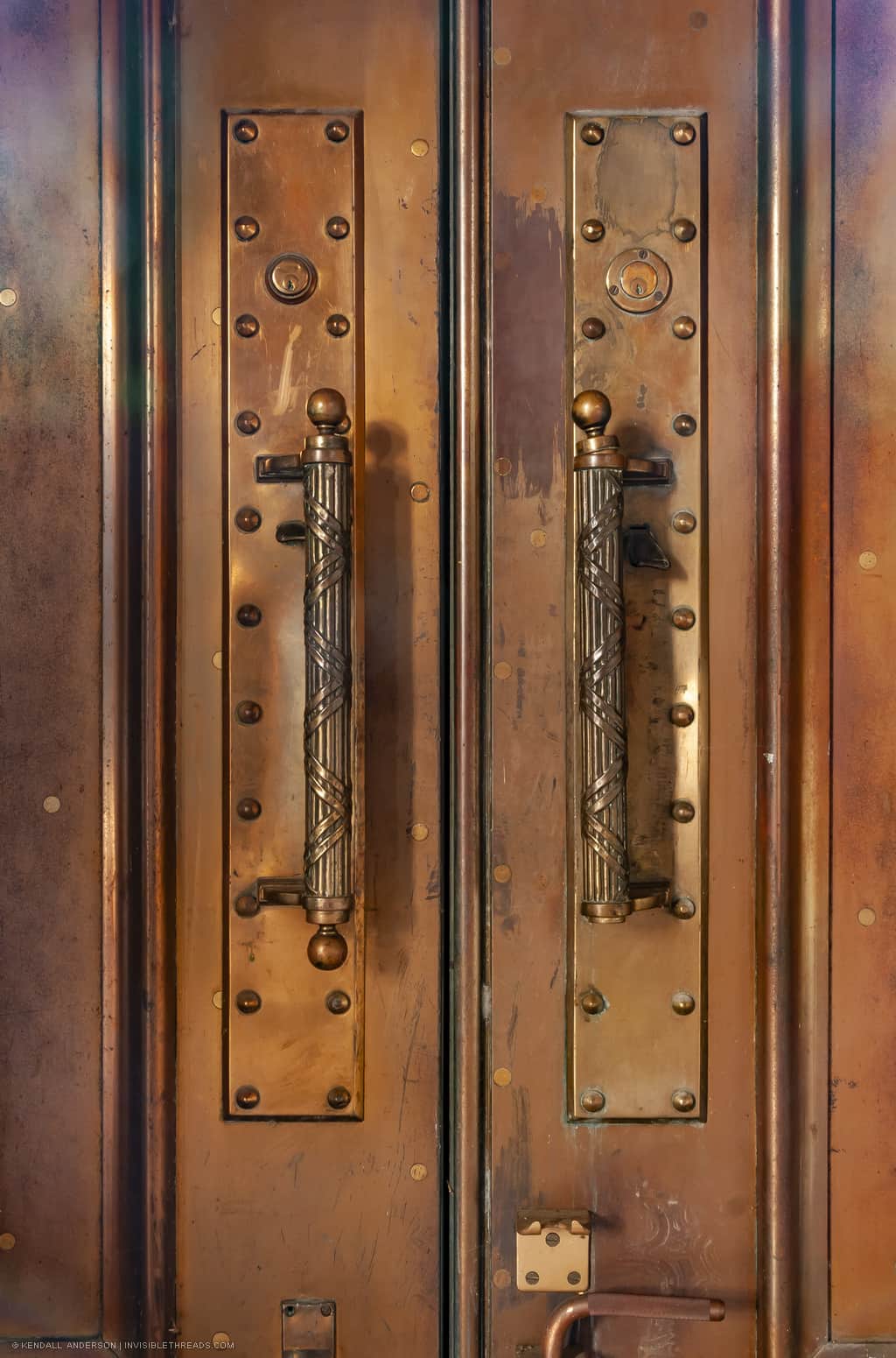 Ornate solid brass door handles are mounted on plates on solid copper doors.