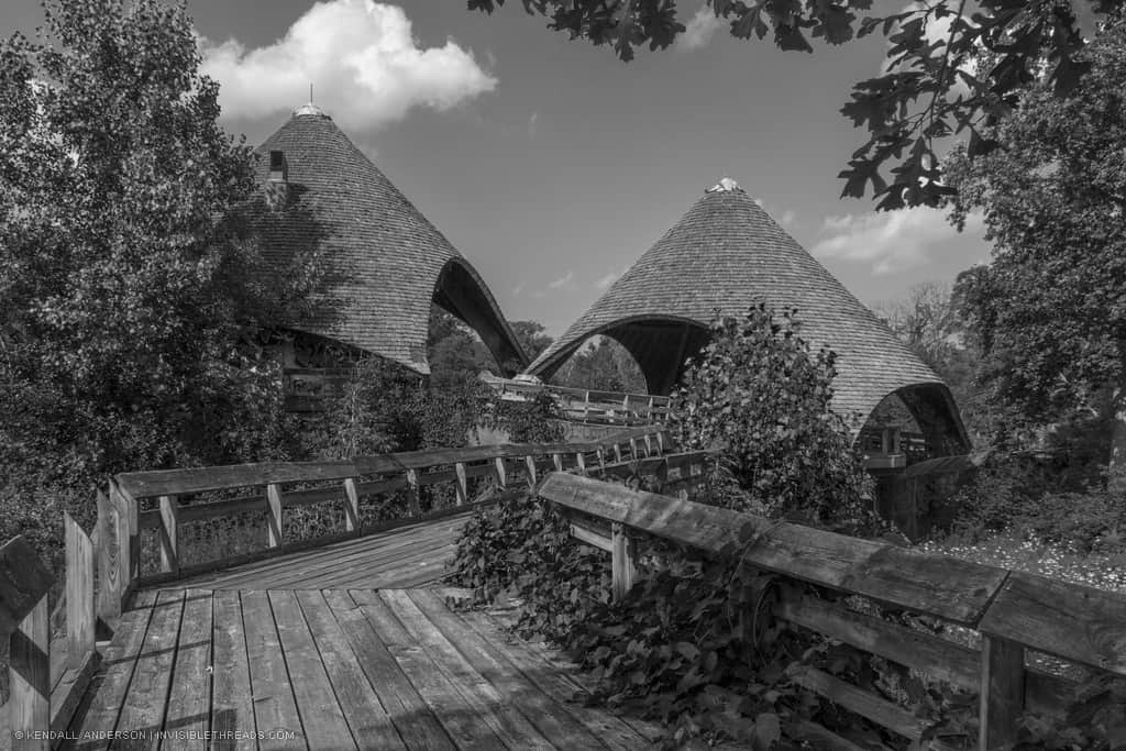 Two built pyramid-like cone structures covered in shingles, at the end of a wooden boardwalk, in an overgrown forest