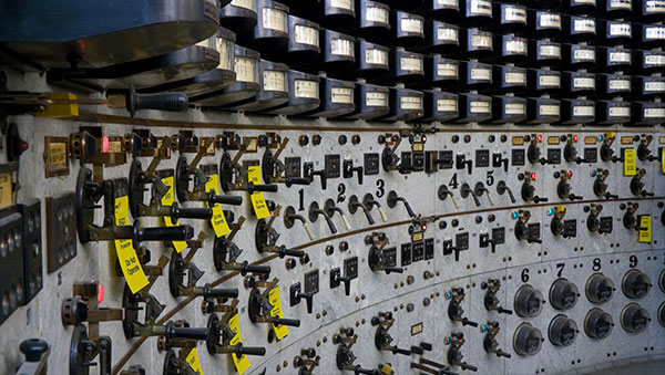 The control room has a curved marble wall. A large array of ammeters, knobs and levers are mounted on the marble wall and are visible from the main desk.